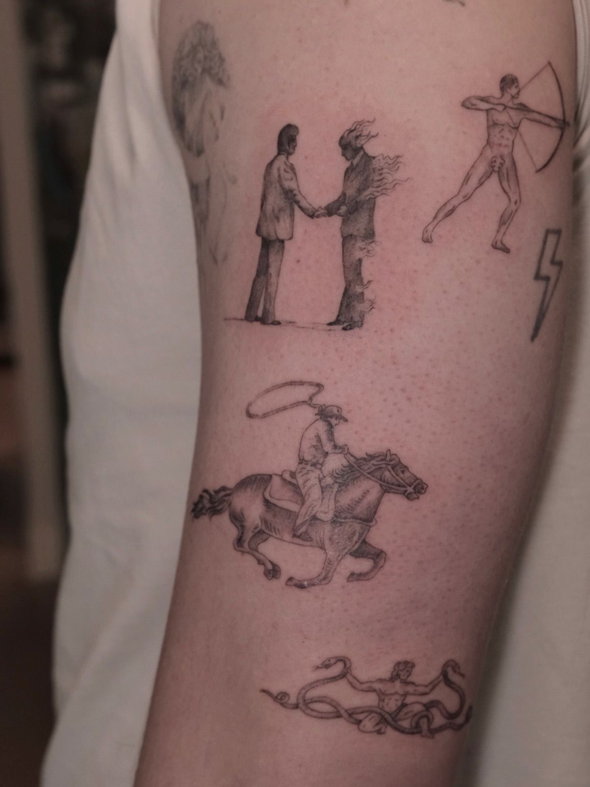 Arm covered in fine line western scenes: a handshake, a rider on horseback, an archer